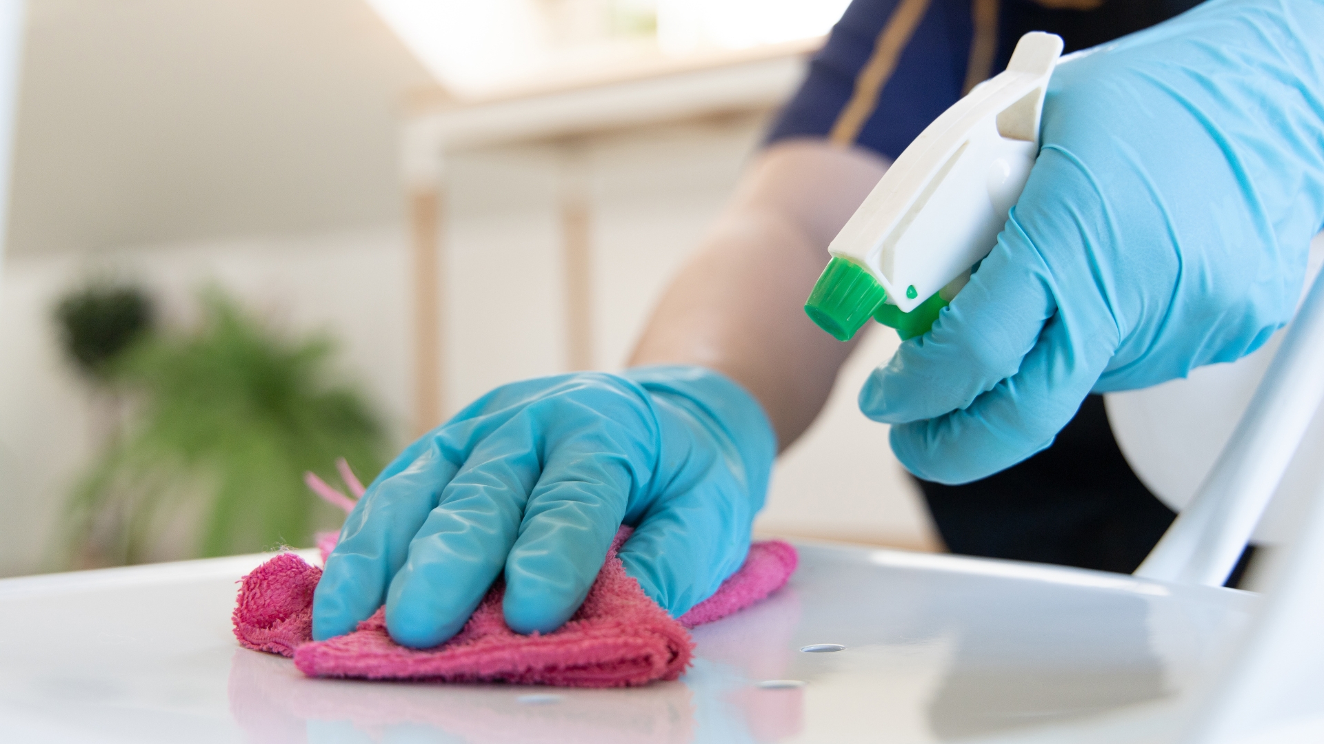 A person in blue gloves is cleaning a table